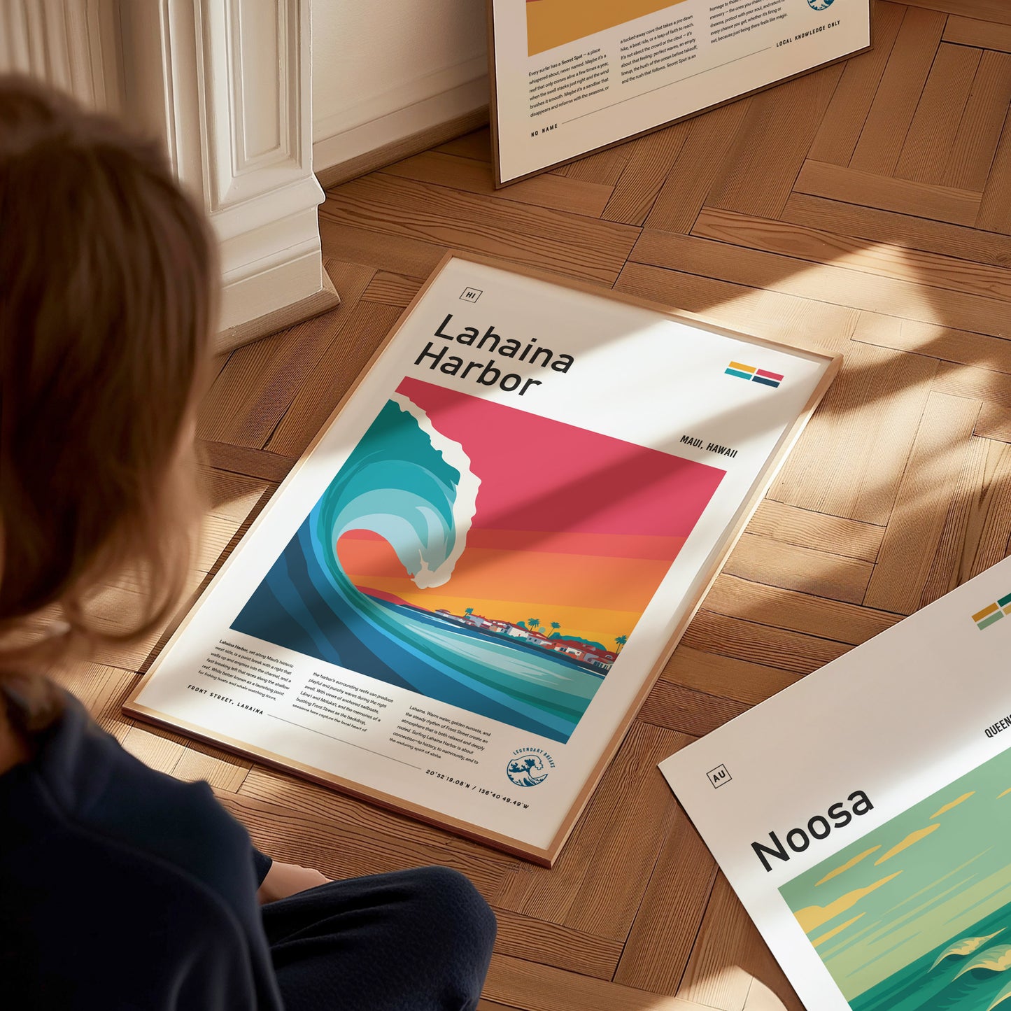 A person sits on a wooden floor, gazing at a colorful poster featuring a stylized wave and vibrant sunset over Lahaina Harbor in Maui, Hawaii. The poster showcases the essence of surf culture with bold colors and artistic design elements.