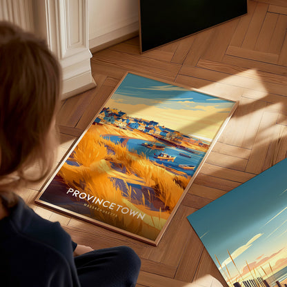 A child sits on a wooden floor, gazing at a framed travel print of Provincetown, depicting a vibrant harbor scene with colorful houses, boats, and golden grass under a bright sky. The artwork captures the lively essence of a seaside town.