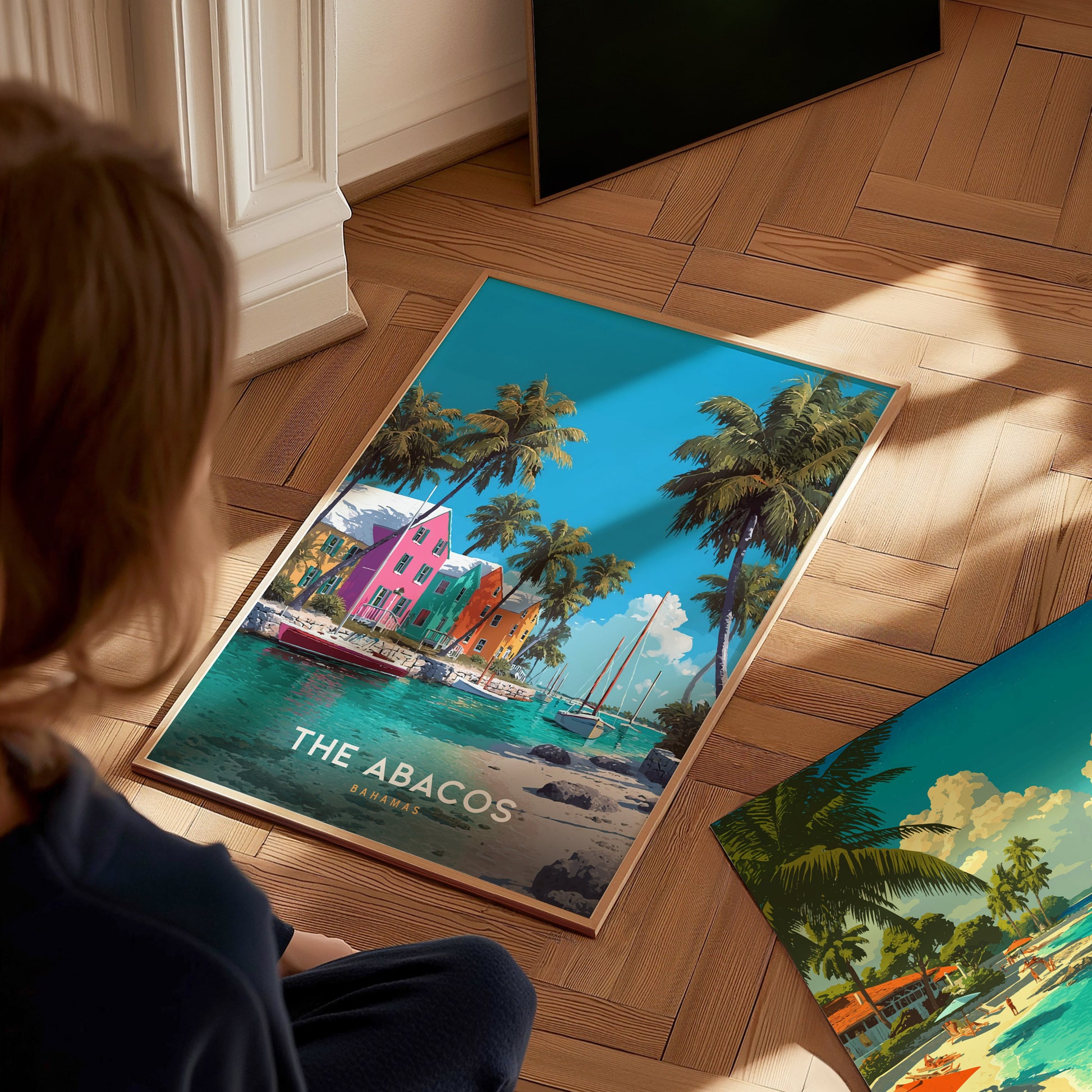 A child sits on a wooden floor, gazing at a colorful travel poster featuring vibrant, pastel-colored buildings along a tropical waterfront. The scene is adorned with palm trees and a bright blue sky, evoking a sunny, beachy atmosphere.