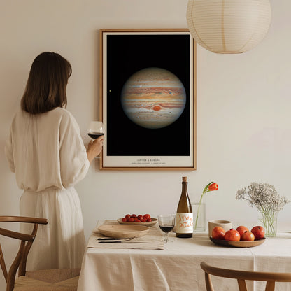 Woman in a white dress standing in a dining room with a framed poster of Jupiter on the wall.