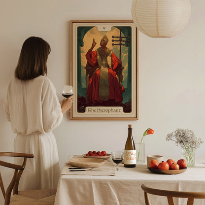 A woman in a white dress holds a glass of wine, admiring a Hierophant tarot poster on the wall. A table with fruit, wine, and flowers is in the foreground.