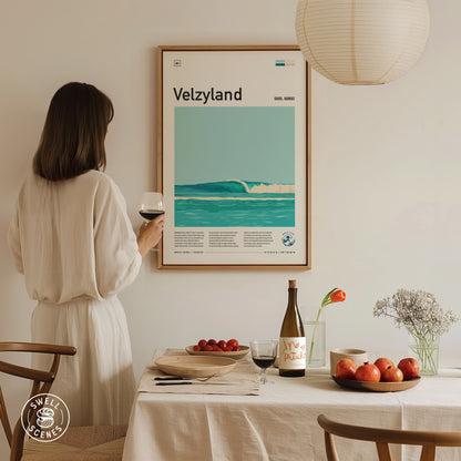 A woman in a white dress gazes at a framed Velzyland surf poster on a wall. The table beneath holds wine, tomatoes, apples, and flowers, creating a cozy dining scene.