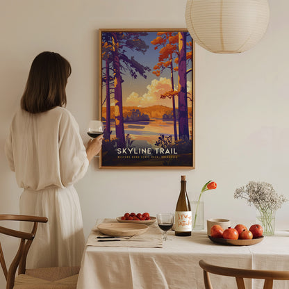 A woman in a white dress admires a colorful Skyline Trail poster on a wall. A table with wine, apples, and flowers is set in the foreground.