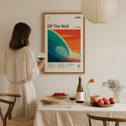 A woman in a light-colored, flowing dress holds a glass of wine while admiring a colorful poster titled Off The Wall, featuring a stylized wave against a sunset backdrop.