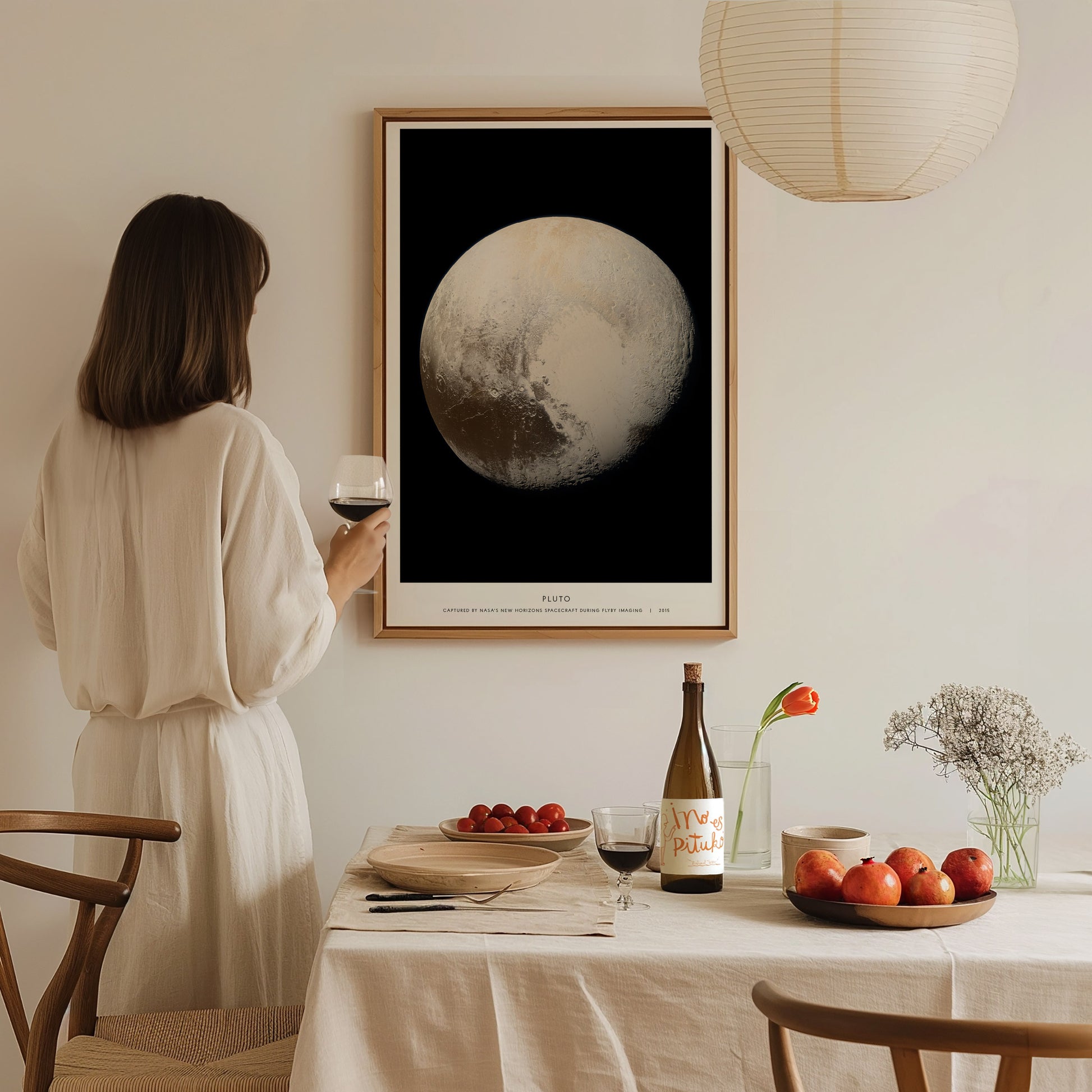 Woman in a white dress standing in a dining room with a large framed Pluto poster on the wall.