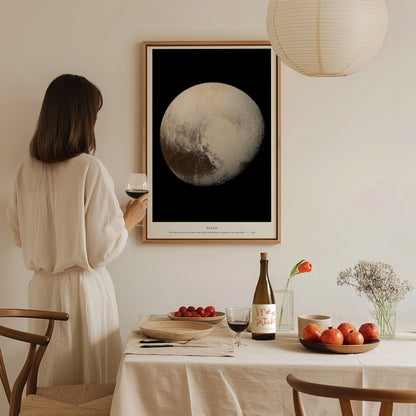 Woman in a white dress standing in a dining room with a large framed Pluto poster on the wall.