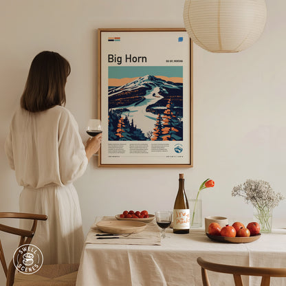 A person in a white dress holds a wine glass, admiring a framed Big Horn ski run poster on the wall.