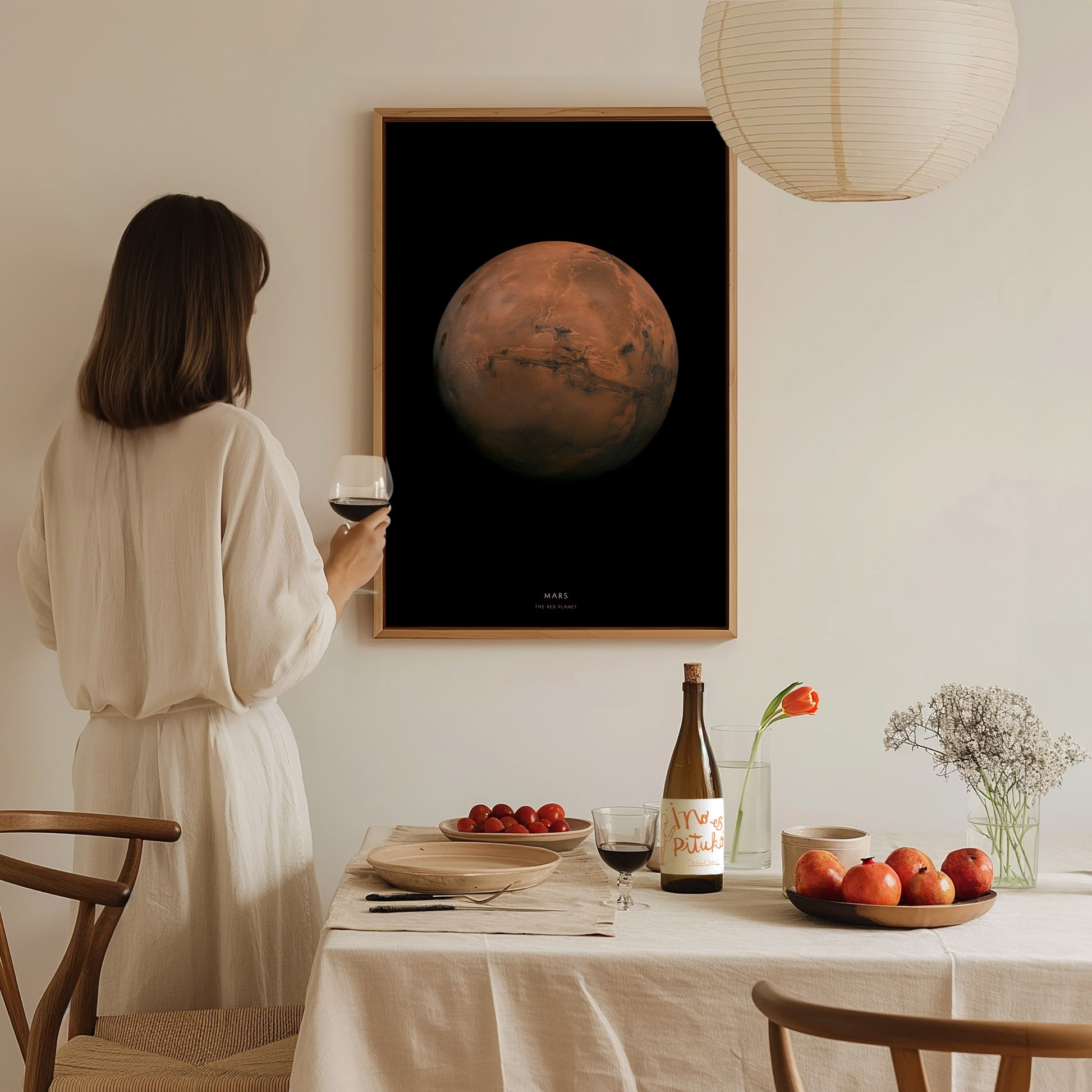 Woman in a white dress standing in a dining room with a framed image of Mars on the wall.