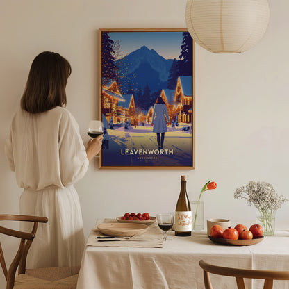 A woman in a white dress admires a framed Leavenworth Washington poster on a wall. A dining table with wine, fruits, and flowers is in the foreground.