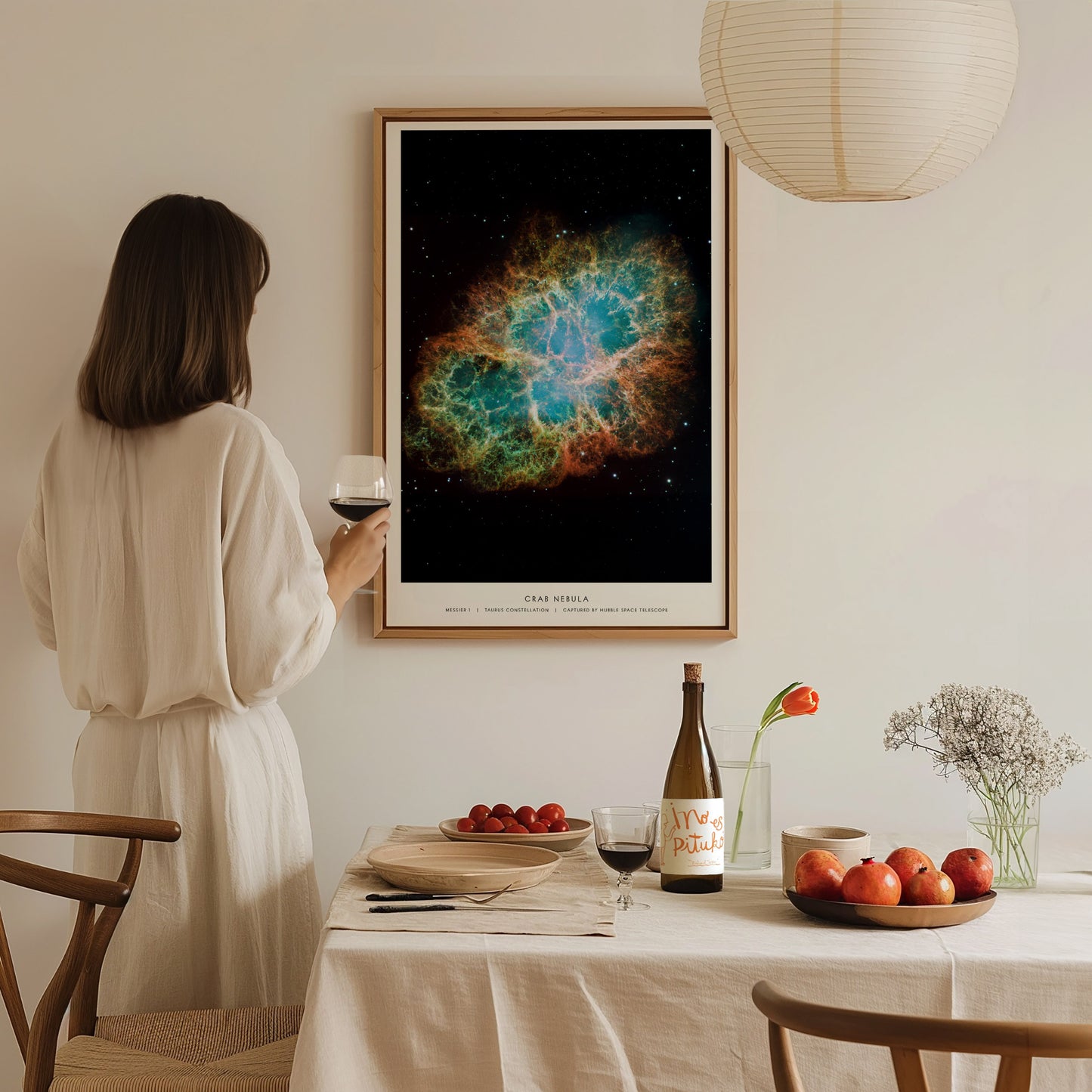 Woman in a white dress standing in a dining room with a framed nebula art print on the wall.