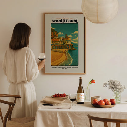 Woman in a white dress standing in a dining room with a framed poster of the Amalfi Coast.