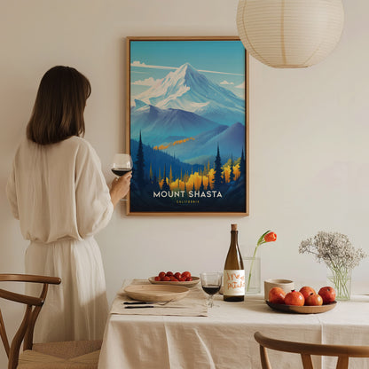 A woman in a light dress holds a wine glass while admiring a Mount Shasta poster. The dining table is set with fruit, wine, and flowers, creating a cozy atmosphere.