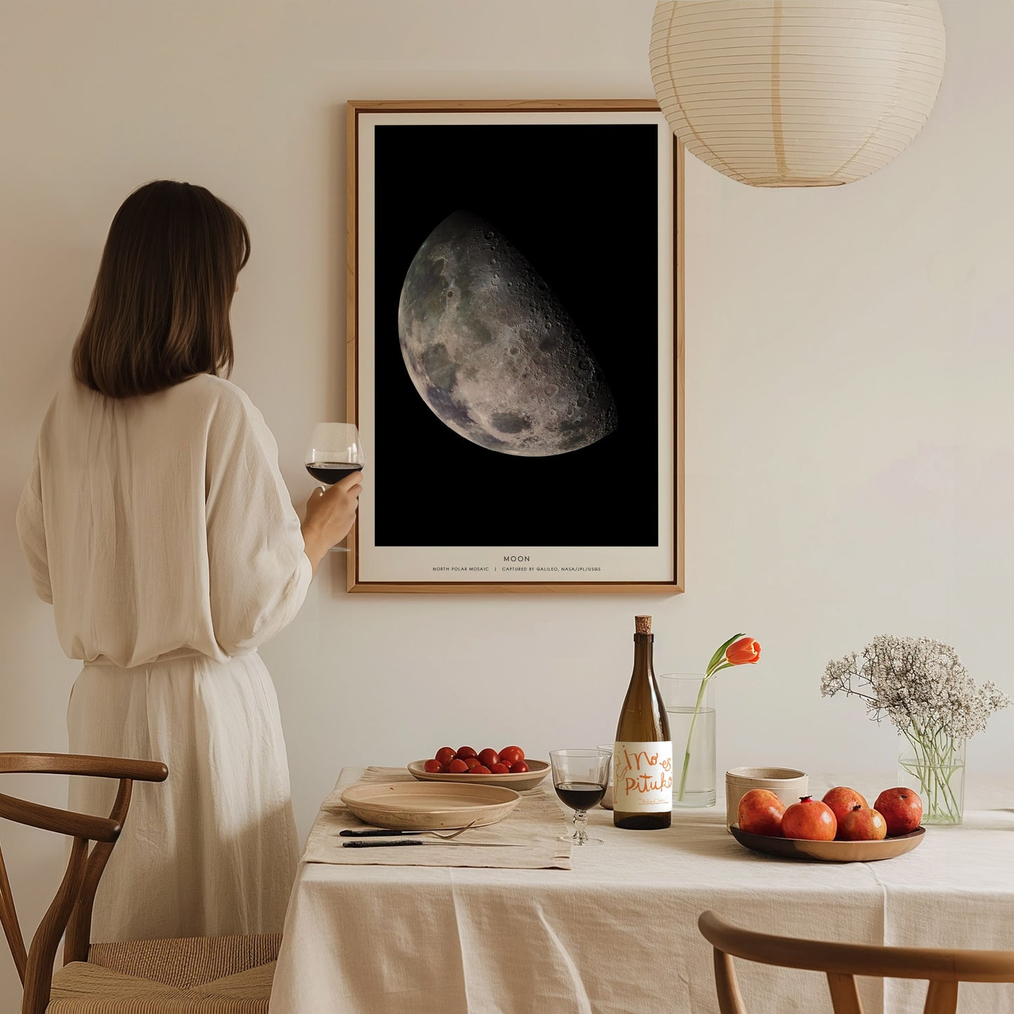 Woman in a white dress standing in a dining room with a framed moon poster on the wall.