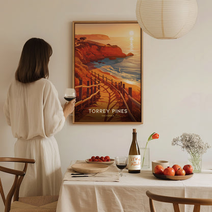 A person in a white dress holds a glass of wine, gazing at a Torrey Pines poster. A dining table with fruit, wine, and flowers is in the foreground.