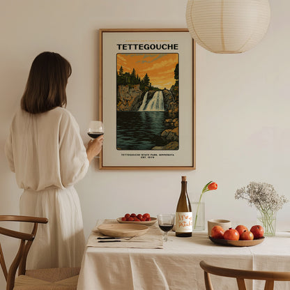 A woman in a white dress holds a glass of wine, admiring a Tettegouche State Park poster. The scene includes a set dining table with fruit and wine.