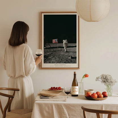 Woman in a white dress standing in a dining room with a framed photograph of an astronaut on the moon.
