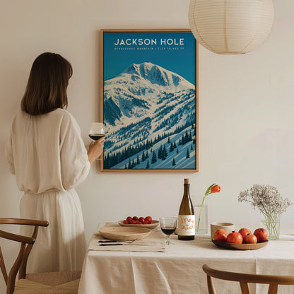 A woman in a white dress stands beside a dining table, admiring a framed travel poster of Rendezvous Mountain in Jackson Hole. The artwork features snowy peaks and pine trees, enhancing the cozy atmosphere of the room.