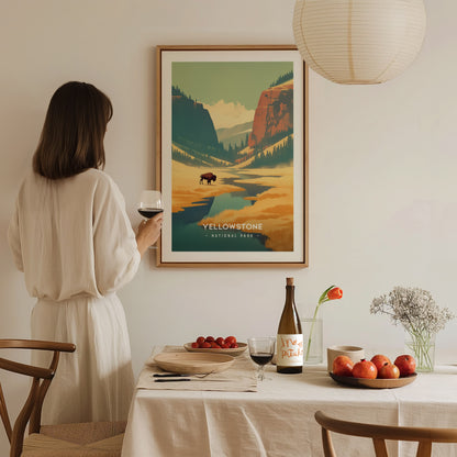 A woman in a white dress holds a wine glass while admiring a Yellowstone National Park poster. The table is set with fruit, a wine bottle, and flowers.