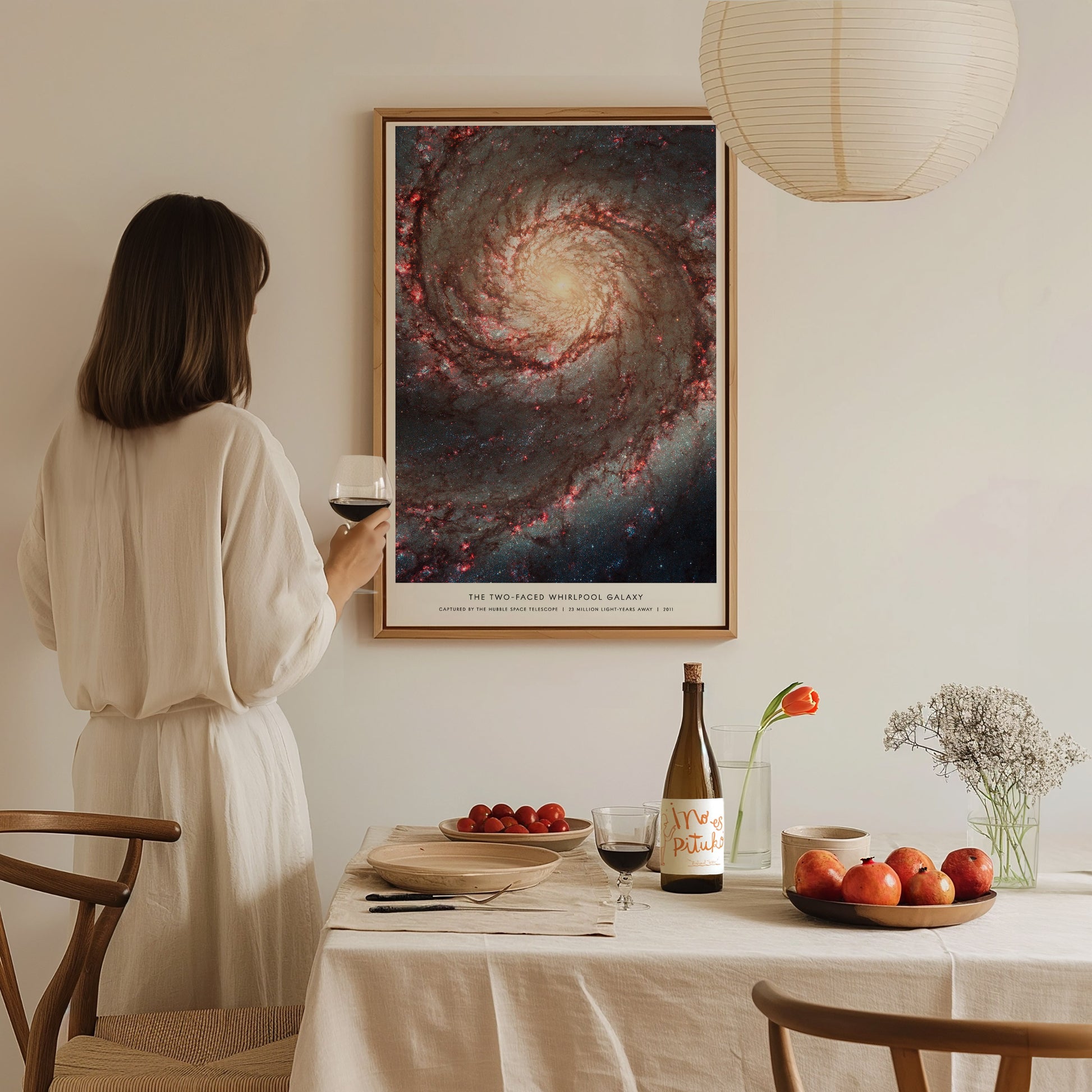 Woman in a white dress standing in a dining room with a large framed poster of a galaxy on the wall.