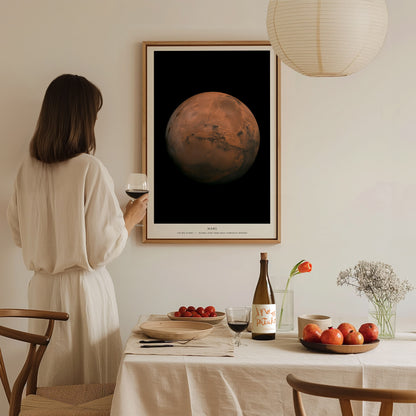 Woman in a white dress standing in a dining room with a framed image of Mars on the wall.