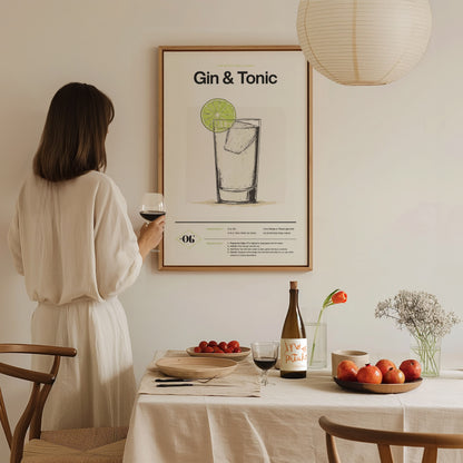 A woman in a white dress holds a wine glass, gazing at a framed Gin & Tonic poster on a wall above a dining table with fruits and flowers.