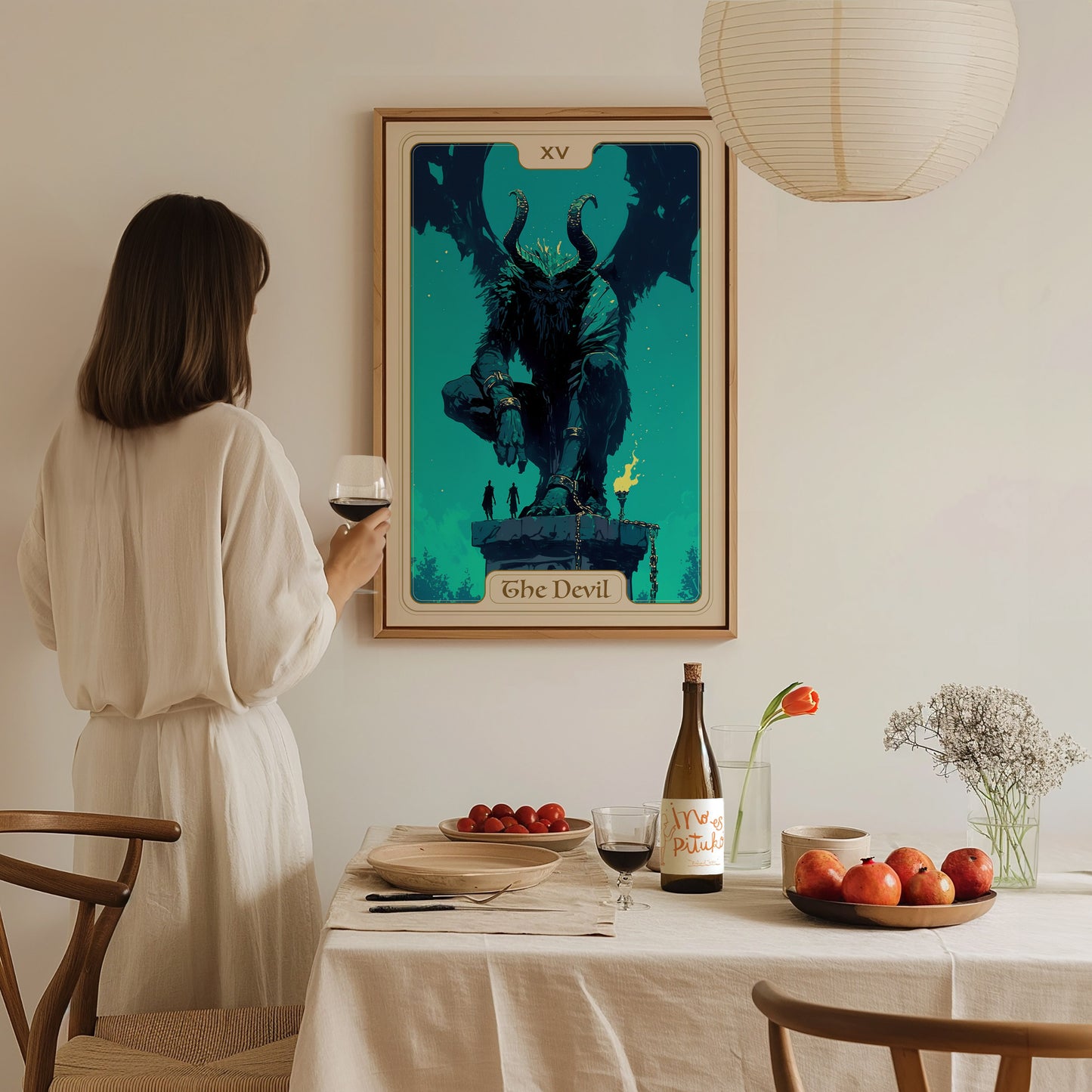 A person in a light-colored, flowing outfit stands at a dining table, holding a glass of wine. Behind them, a framed poster of the Devil Tarot card, featuring a dark, horned figure, is displayed on the wall, adding a mystical touch.