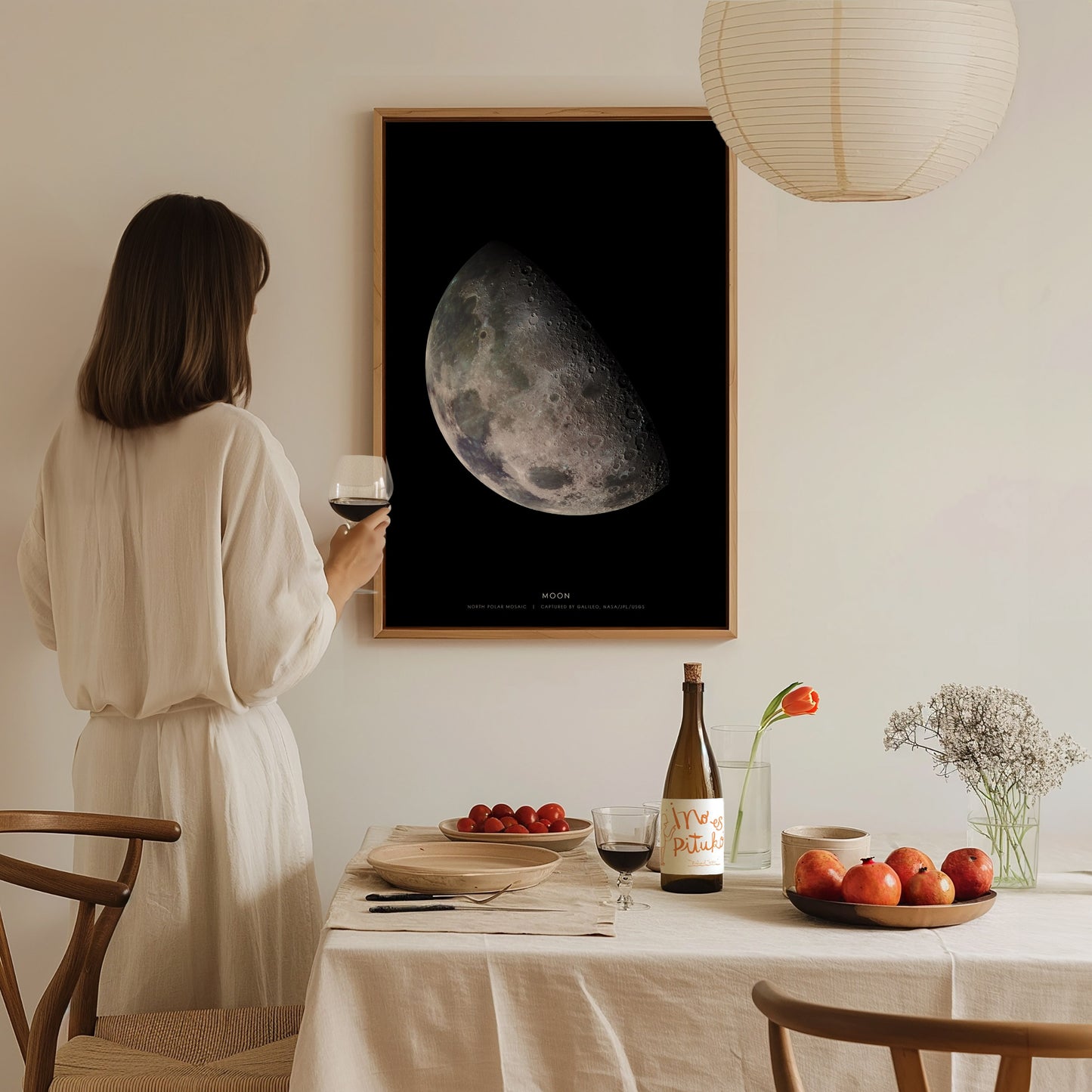 Woman in a white dress standing in a dining room with a large moon poster on the wall.