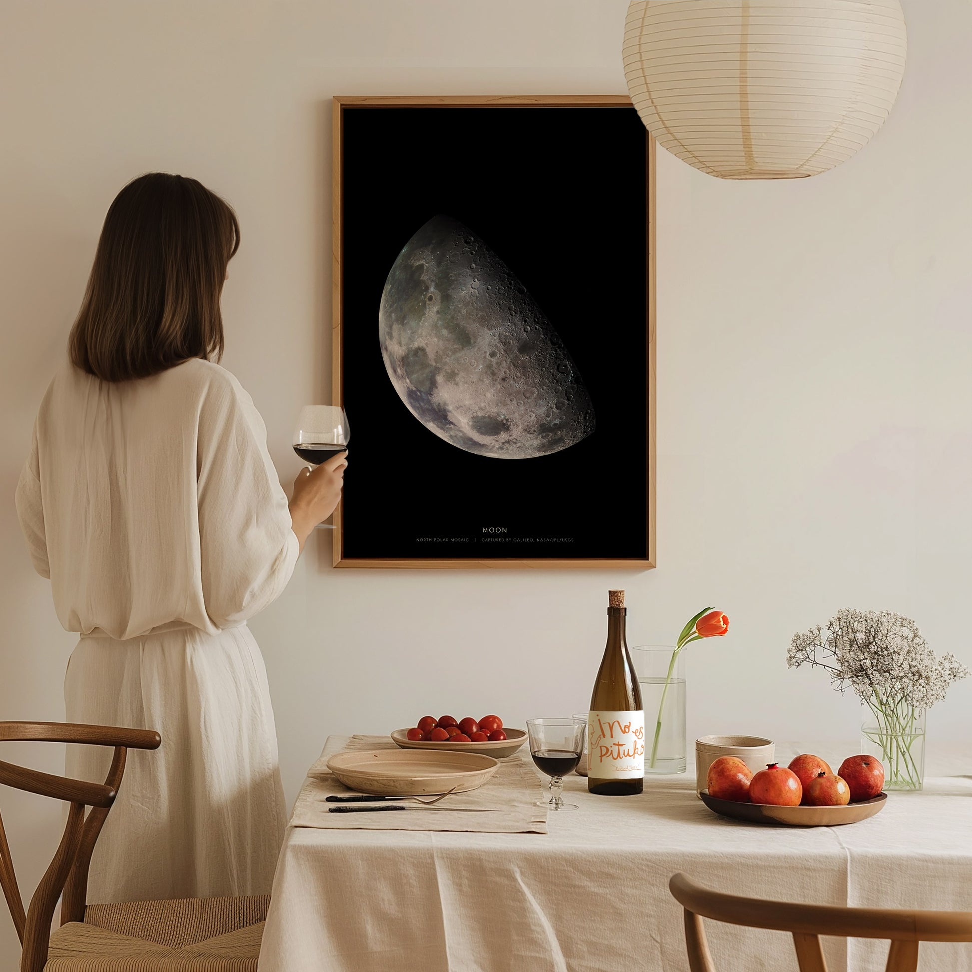 Woman in a white dress standing in a dining room with a large moon poster on the wall.