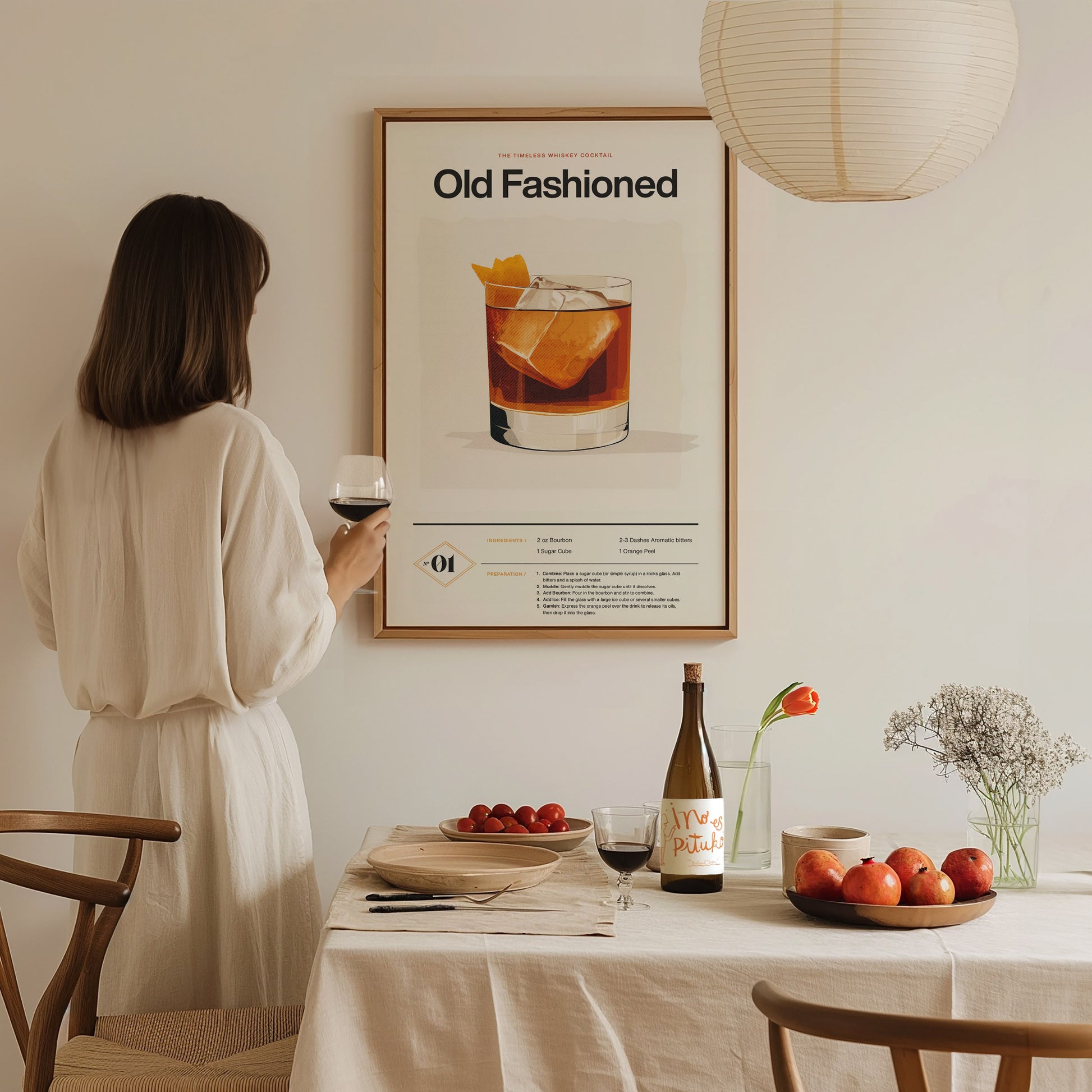 A woman in a white dress holds a glass of wine, looking at an Old Fashioned cocktail poster. A table with fruit, wine, and flowers is in the foreground.