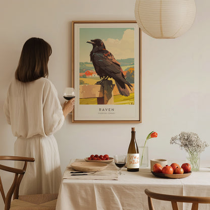 A woman in a white dress stands holding a glass of wine while gazing at a framed art print of a raven perched on a fence. The scene is set in a cozy, minimalist dining area with a table adorned with fruits and a bottle of wine.