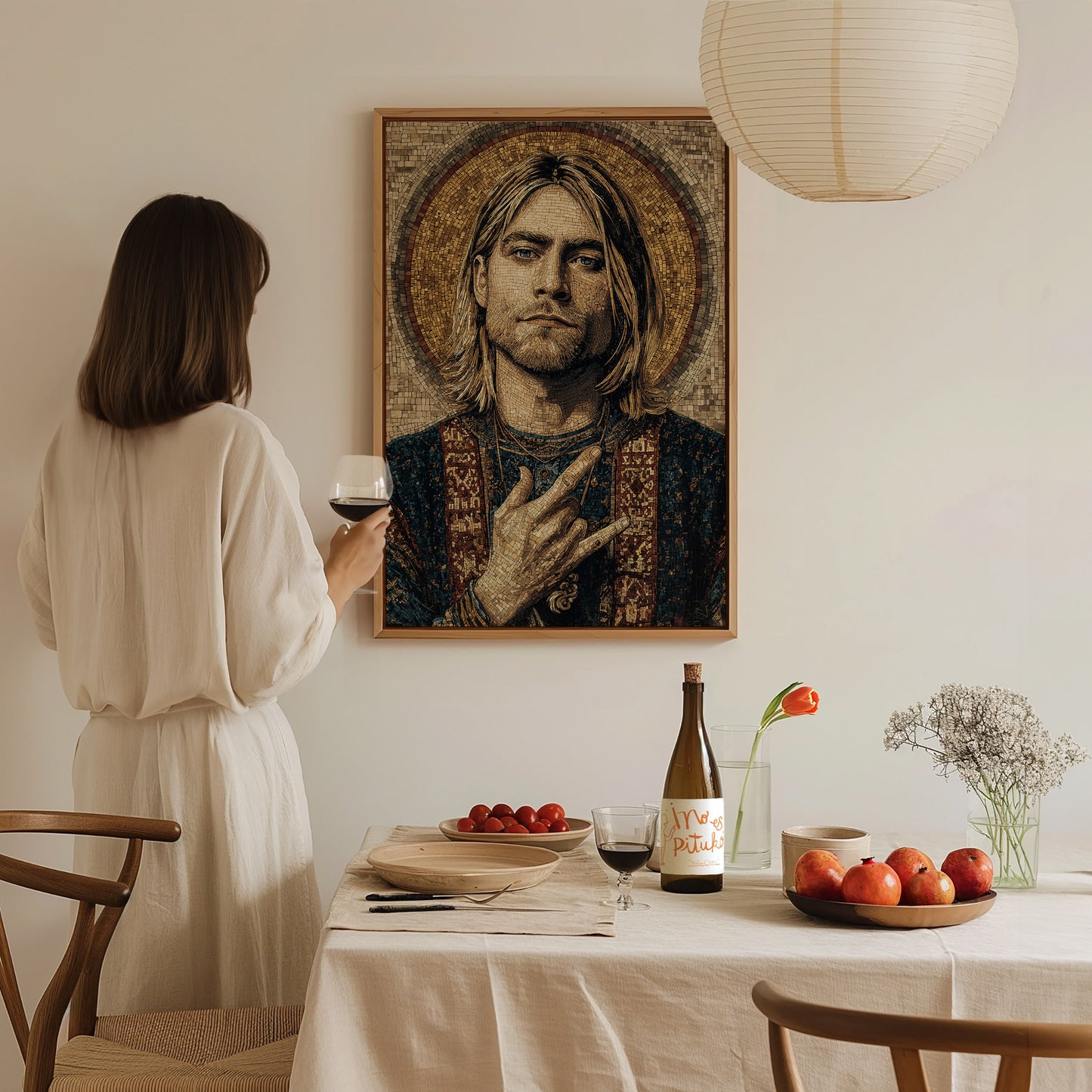 A woman in a white outfit stands at a dining table, holding a glass of wine and gazing at a framed mosaic portrait of a musician on the wall.
