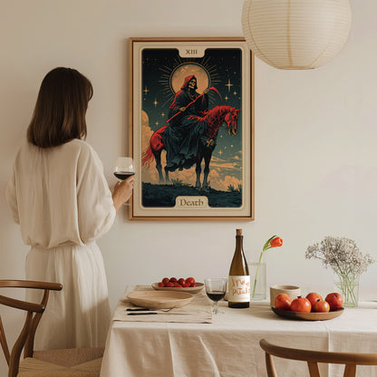 A woman in a white dress holds a wine glass, gazing at a framed Death tarot card poster on the wall. The table is set with fruits, a bottle, and.